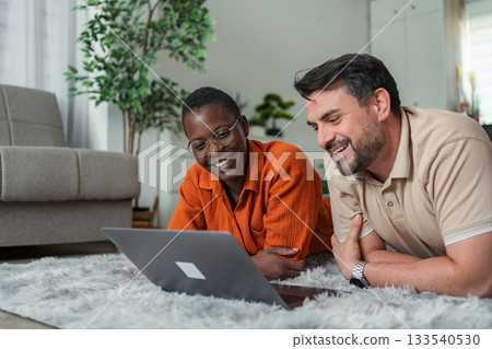 Happy couple lying on carpet using laptop at home Happy couple lying on carpet using laptop at home 133540530