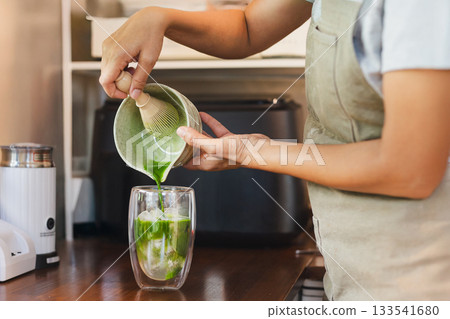 Barista pouring Matcha to a glass of ice with traditional japanese matcha. 133541680