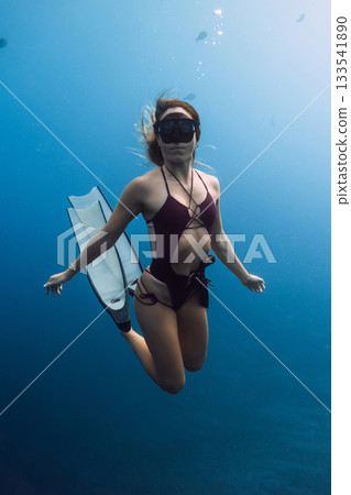 Woman freediver gracefully swims underwater with freediving fins in blue ocean Woman freediver gracefully swims underwater with freediving fins in blue ocean 133541890