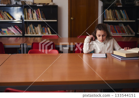 Young Girl Studying At Library Table With Books And Notepad 133544151