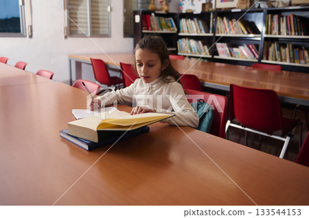 Young Student Studying At Library Table With Books In School, Quiet Learning Moment 133544153