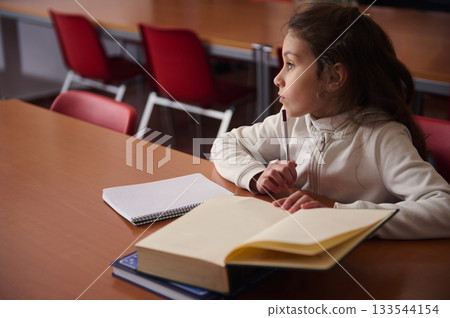 Young Student Focused In Classroom Library Studying With Book And Notebook During School Time Today 133544154