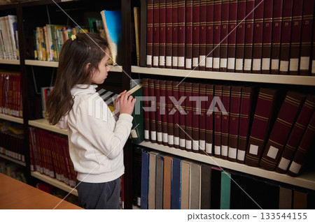 Young Girl Exploring Books in a School Library During Study Time and Learning Young Girl Exploring Books in a School Library During Study Time and Learning 133544155