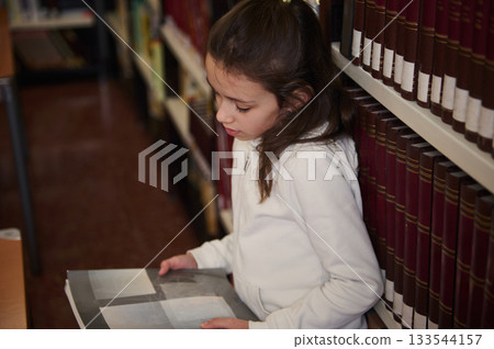 Young Girl Reading a Book in a Library Aisle Exploring Knowledge and Learning Young Girl Reading a Book in a Library Aisle Exploring Knowledge and Learning 133544157