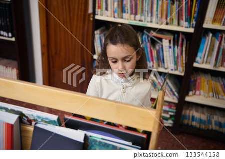 Young Girl Reading Books in Library Aisle During Back To School Day 133544158
