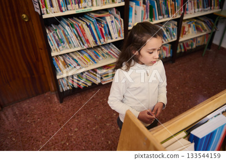 Young Girl In Library Exploring Books During A School Day Focused On Knowledge and Learning 133544159