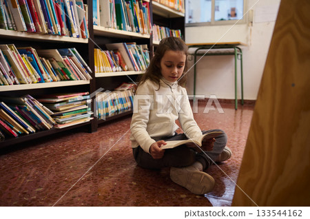 Young Girl Reading a Book in a School Library, Focused on Learning and Knowledge 133544162