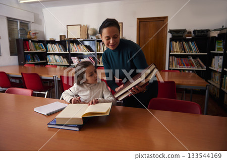 Teacher Assists Child With Books In Public Library During Study Session 133544169