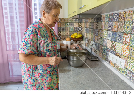 An elderly woman is preparing food in the kitchen at home. 133544360