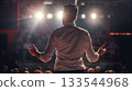 A man seen from behind speaks to an audience, his arms open wide under the spotlight, engaging the crowd in a seminar or event. 133544968