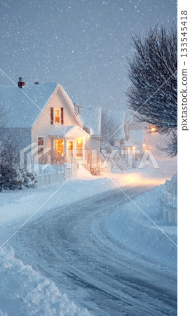 serene winter scene shows a snow-covered street and white houses with warmly lit windows under a soft snowfall 133545418