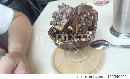 Chocolate ice cream sundae with brownie pieces and almond flakes in glass bowl, indulgent dessert moment 133546511