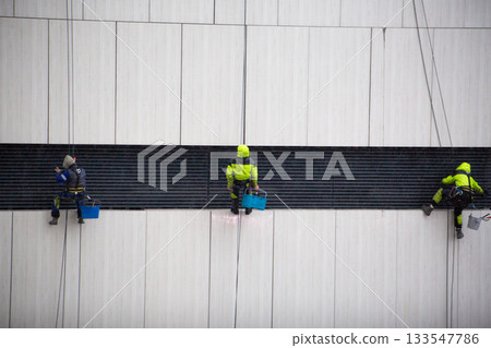 Team of industrial climbers works on wall of building. Cleaning ventilation and exhaust ducts with help of professional climbers. This is difficult and dangerous job with risk to life 133547786