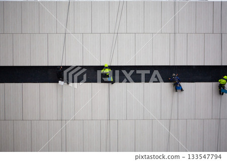 Industrial climbers at work. Cleaning building facade after construction. Dangerous profession at height during adverse weather conditions. Professional climbers in risky job 133547794