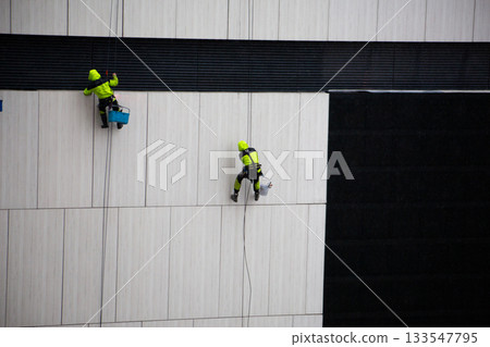Industrial climber descends the side of building in poor weather. Harsh weather conditions during work at height. Dangerous profession with risk to life Industrial climber descends the side of building in poor weather. Harsh weather conditions during work at height. Dangerous profession with risk to life 133547795
