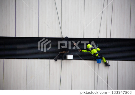 Cleaning building exterior supply system with industrial climbers. Heavy work at height. Day work for industrial climber. Overcoming your fear of heights for job Cleaning building exterior supply system with industrial climbers. Heavy work at height. Day work for industrial climber. Overcoming your fear of heights for job 133547803