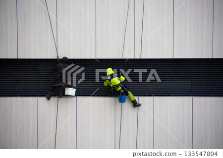 Poor weather conditions during work at height. Industrial climbers clean the building facade. Working at height on ropes with safety equipment Poor weather conditions during work at height. Industrial climbers clean the building facade. Working at height on ropes with safety equipment 133547804