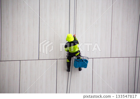 Industrial climber in bright suit descends using safety ropes after completing work at height. The industrial climber work is complete. Ending the workday at height 133547817
