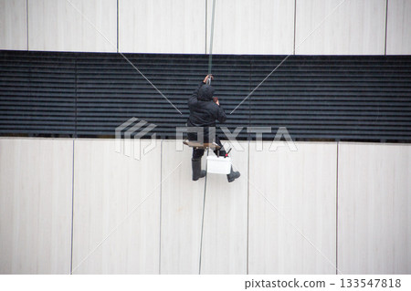 Industrial climber checks safety carabiner during dangerous work at height. Life threatening profession. The process of performing facade work with the help of climber 133547818