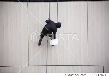 Industrial climber stores his tools while working at height. Risky climber procession during industrial activities. Male climber hangs from safety ropes while working Industrial climber stores his tools while working at height. Risky climber procession during industrial activities. Male climber hangs from safety ropes while working 133547821