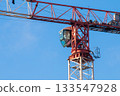 Close-up view of Control Cabin and Boom Section of Red-and-white Tower Crane on Construction Site against Blue Sky on Sunny Day. Fasteners of Crane and Metal Parts are covered with Rust 133547928