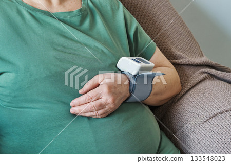 An elderly woman using digital wrist monitor to measure blood pressure Close-up 133548023