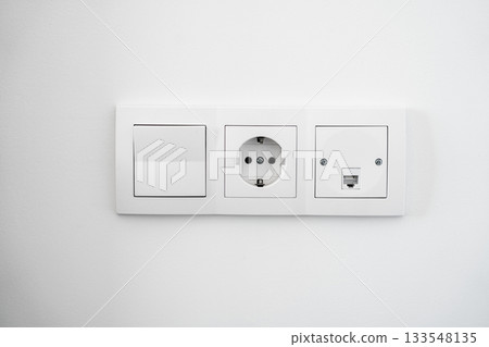 Modern white wall switch and electrical socket panel installed on clean interior surface in bright room 133548135