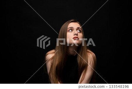 Studio portrait of young woman looking upward with thoughtful expression on black background 133548196