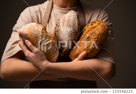 Baker holding three artisan bread loaves, showcasing variety, texture, and handcrafted quality Baker holding three artisan bread loaves, showcasing variety, texture, and handcrafted quality 133548225