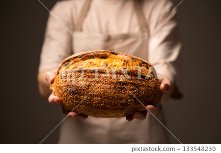 Baker holding seeded artisan loaf with raisins and golden crust Baker holding seeded artisan loaf with raisins and golden crust 133548230
