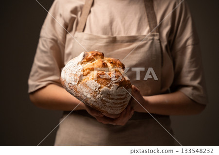 Artisan baker holding freshly baked rustic sourdough loaf in warm soft light Artisan baker holding freshly baked rustic sourdough loaf in warm soft light 133548232