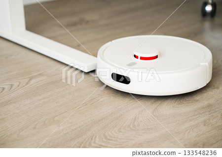 Robot vacuum cleaner moving under table while cleaning wooden floor with precise smart navigation system 133548236