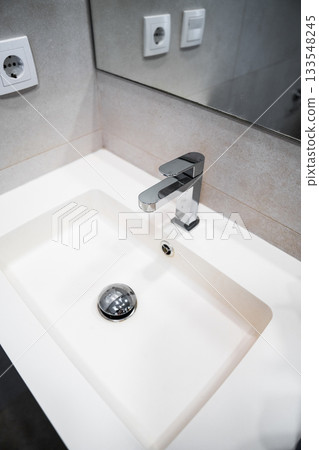 Modern bathroom sink with chrome faucet and mirror reflecting minimalist clean interior design details 133548245