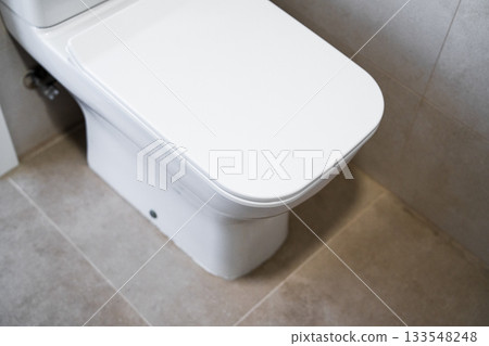 Modern white toilet with closed lid in clean tiled bathroom interior with soft lighting 133548248