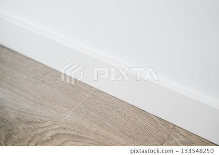 White baseboard detail with wooden textured flooring in clean minimalist interior space White baseboard detail with wooden textured flooring in clean minimalist interior space 133548250