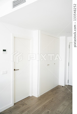 Bright modern hallway with white door, built-in wardrobe and wood flooring in minimalist apartment design 133548252