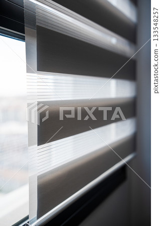 Layered zebra blinds close-up showing soft daylight filtering through translucent and opaque fabric bands Layered zebra blinds close-up showing soft daylight filtering through translucent and opaque fabric bands 133548257