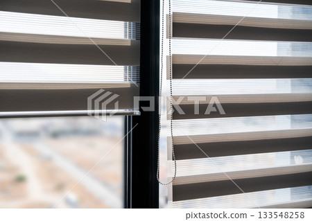 Modern zebra blinds partially open on a tall window with bright outdoor view softened by layered fabric panels Modern zebra blinds partially open on a tall window with bright outdoor view softened by layered fabric panels 133548258