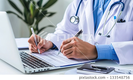 A healthcare worker examines documents and writes notes while using a laptop in a professional office setting A healthcare worker examines documents and writes notes while using a laptop in a professional office setting 133548756