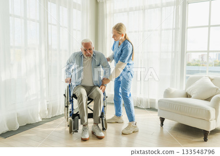 Rehabilitation healthcare. Physiotherapist nurse helps old man patient in wheelchair stand up walking. Man in chair for people with disability doing few steps with nurse helping. Medical caregiver Rehabilitation healthcare. Physiotherapist nurse helps old man patient in wheelchair stand up walking. Man in chair for people with disability doing few steps with nurse helping. Medical caregiver 133548796