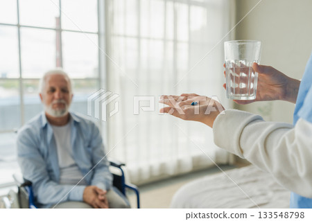 Help support healthcare water balance. Nurse giving glass water for old man patient in wheelchair. Paralyzed man in chair for people with disability drinking fresh water. Senior man and nurse at home 133548798