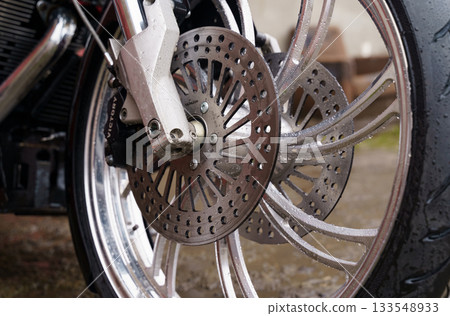 Detailed view of a motorcycle wheel with a shiny brake disc on a rainy day 133548933