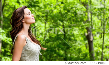 Woman enjoying fresh air in a serene green forest on a sunny day while taking a moment for herself 133549089