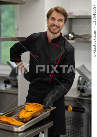 Cook holding tray with pumpkin in oven mitts in professional kitchen 133549557