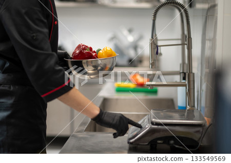 Сhef weighing fresh vegetables on kitchen scale 133549569
