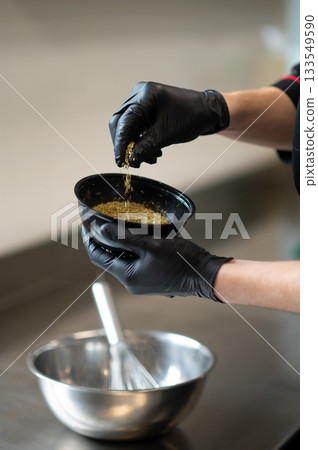 Chef adding spices into metal mixing bowl in professional kitchen Chef adding spices into metal mixing bowl in professional kitchen 133549590