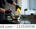 Chef pouring ingredient into metal mixing bowl with whisk 133549596