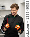 Man in chef uniform displaying sliced bell pepper in kitchen 133549598