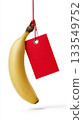 Bright yellow banana hanging from a red tag in a simple setting 133549752