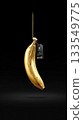 Unique golden banana hanging on a string with a tag against a black background 133549775